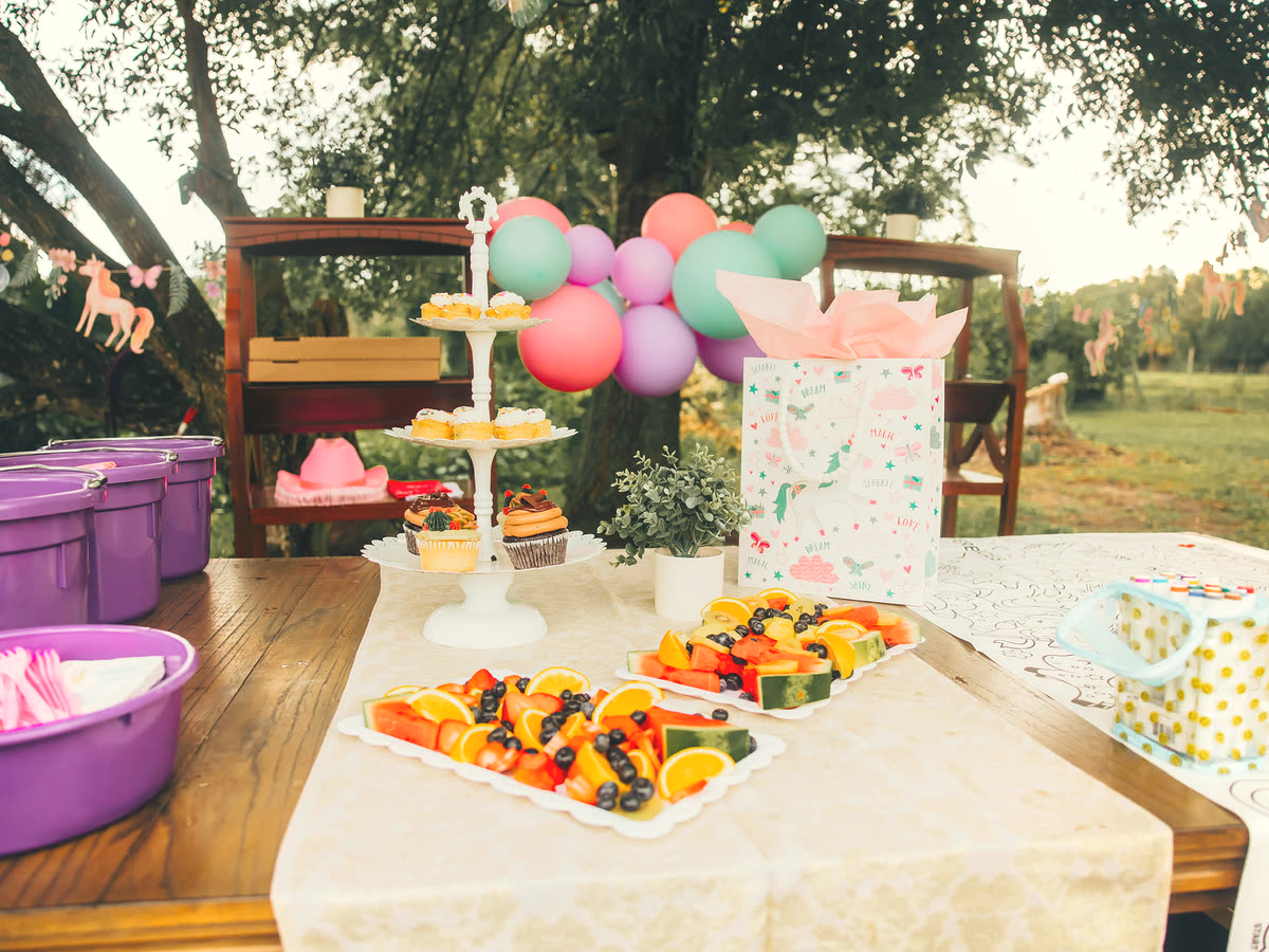 Two children standing with a miniature pony at a backyard party, unicorn bunting overhead